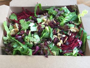 Mixed green salad in food box with nuts and seeds